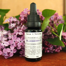 A black bottle with a dropper containing the Blueberry C Serum, labeled for skincare, in front of flowers